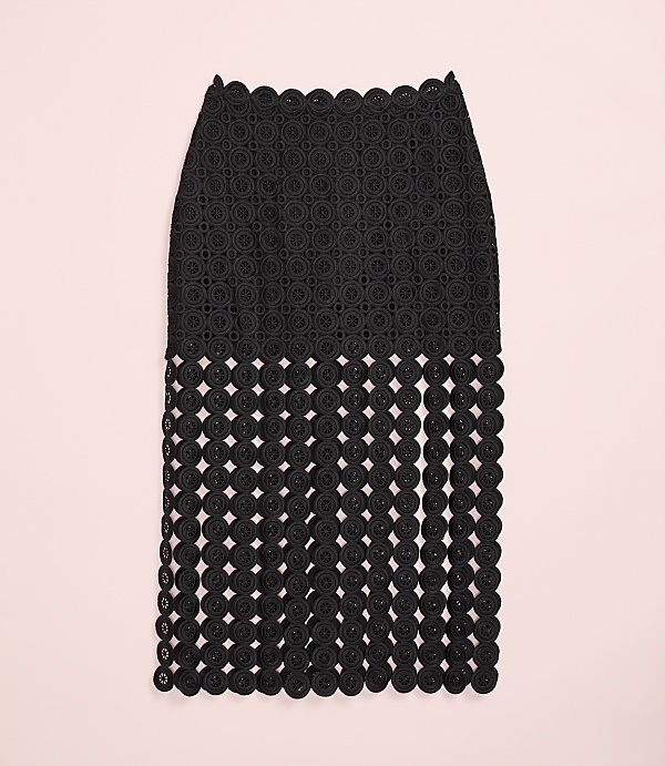 A black, intricately patterned skirt with a fringed bottom hangs against a plain light pink background.