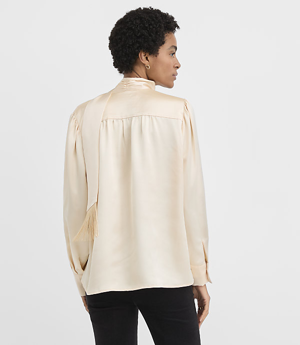 A woman wearing a champagne-colored satin blouse and black pants stands against a plain white background.