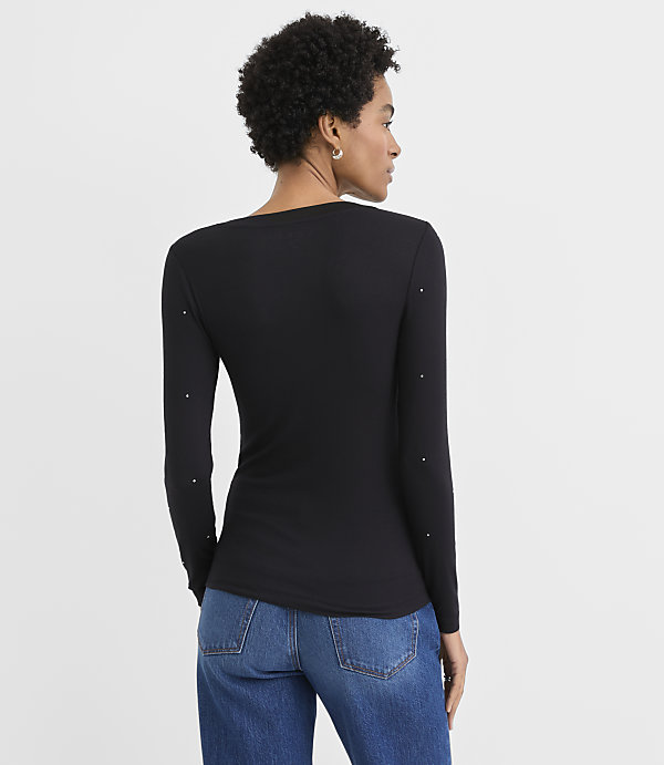 A woman wearing a black long-sleeved top and blue jeans stands with her back to the camera against a plain white background.