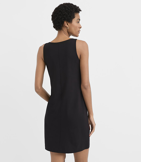 A woman wearing a sleeveless black mini dress stands with her back to the camera against a plain white background.