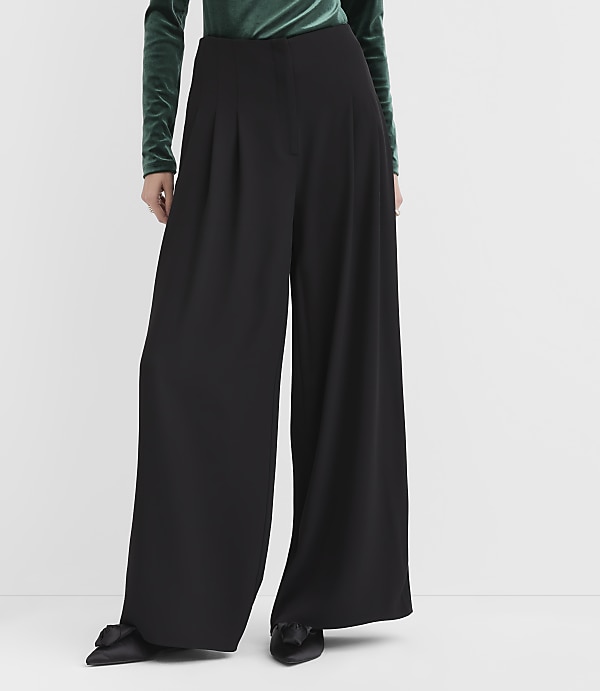 A person wears a green velvet top and wide-leg black trousers against a plain white background.