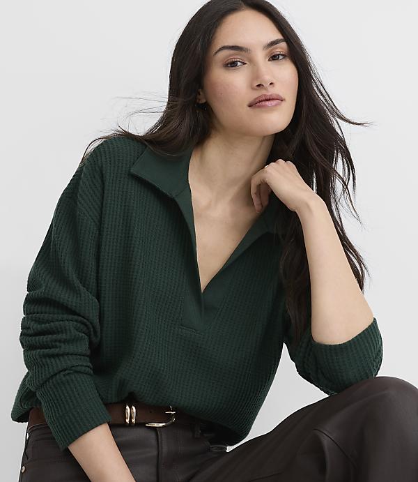 A woman wearing a dark green ribbed polo shirt and brown leather pants poses against a plain white background.