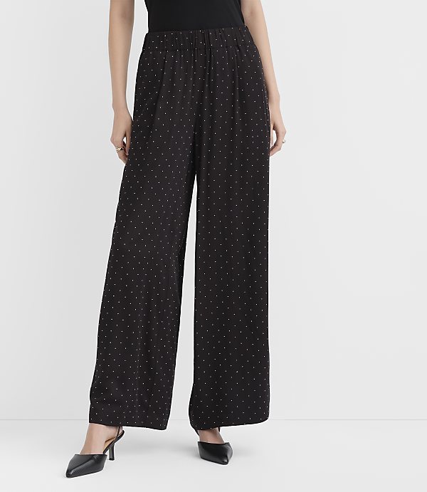 A person wearing black polka-dot wide-leg pants and black heels stands against a plain white background.