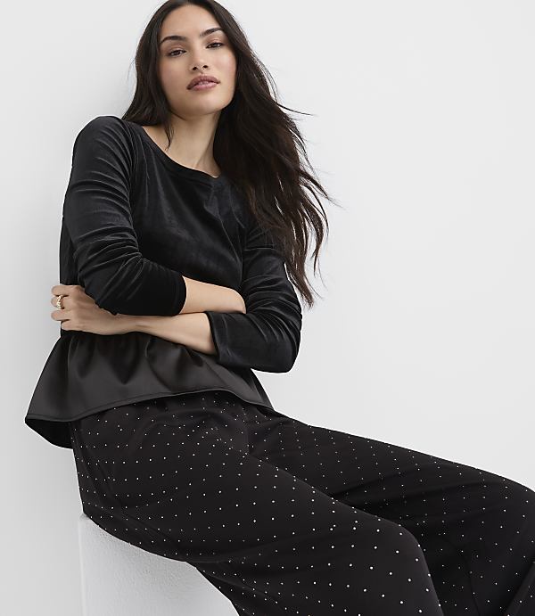 A woman wearing a black velvet top and polka-dot pants sits against a plain white background.