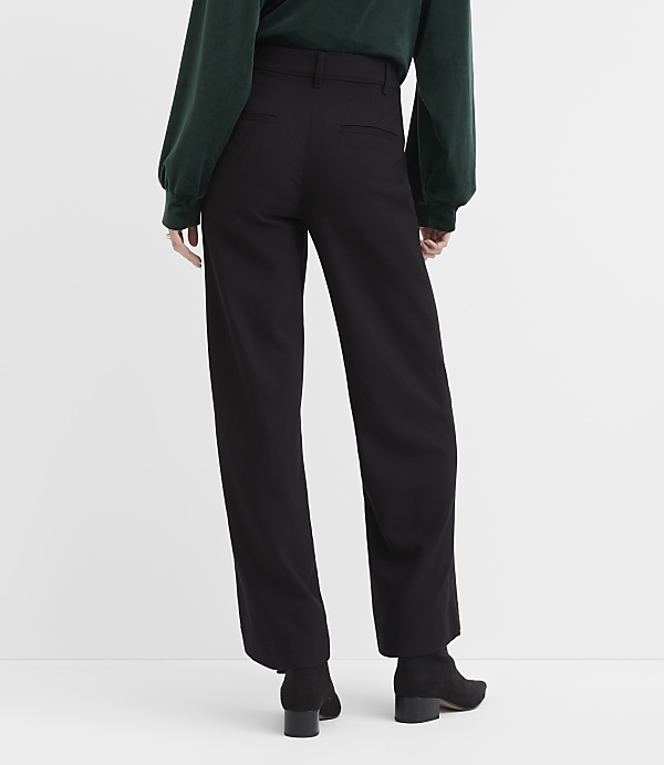 A person wearing a dark green top and black wide-leg trousers stands against a plain white background.