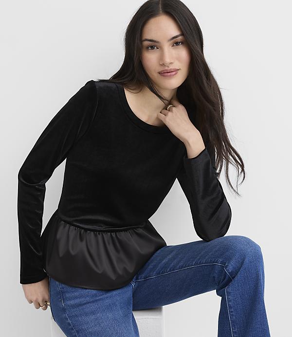 A woman wearing a black velvet top and blue jeans sits against a plain white background.