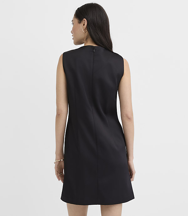 A woman wearing a sleeveless black dress stands with her back to the camera against a plain white background.