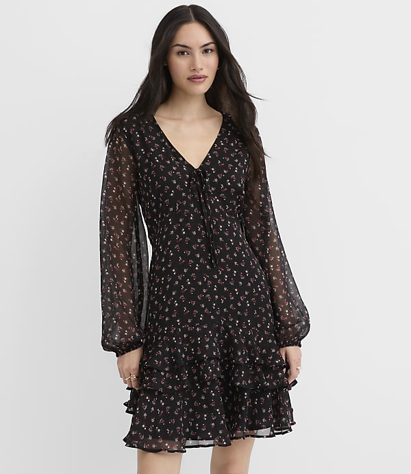 A woman wearing a black floral mini dress stands against a plain white background.