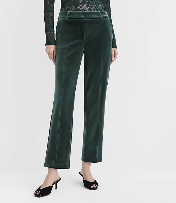 A person wears dark green velvet trousers and a black lace top against a plain white background.