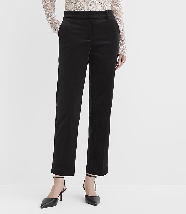 A person wearing a lace top, black trousers, and black pointed-toe heels stands against a plain white background.