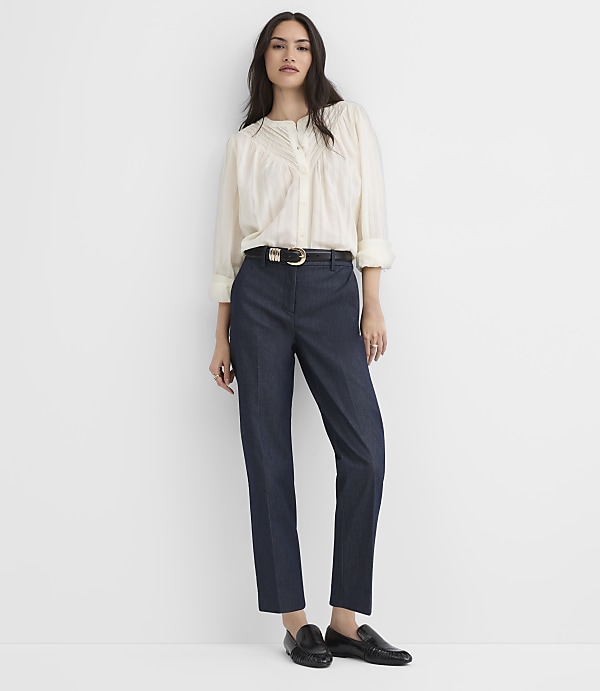 A woman wearing a white blouse, navy trousers, and black loafers stands against a plain white background.