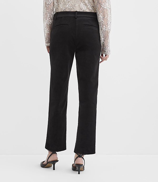 A person wearing a lace top, black trousers, and black heels stands against a plain white background.