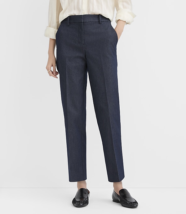 A person wearing a white blouse, navy blue trousers, and black loafers stands against a plain white background.
