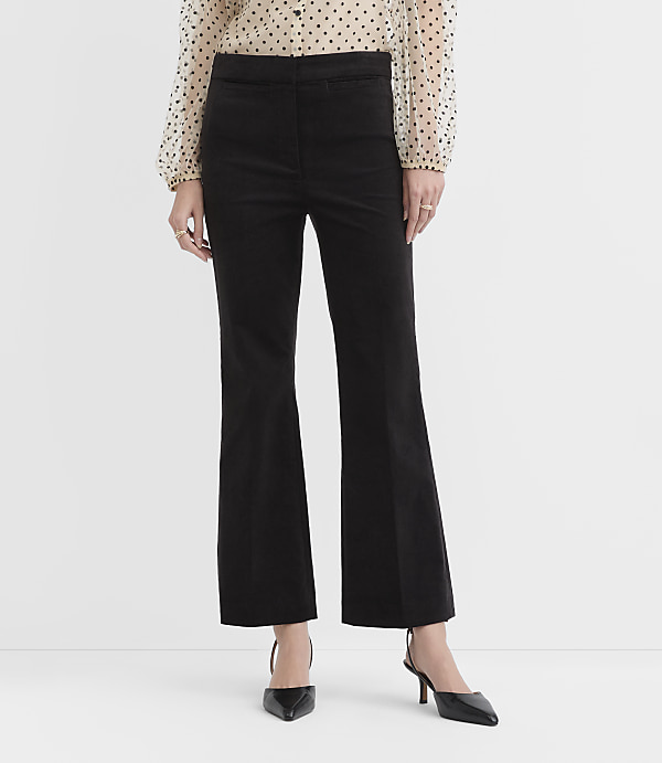 A person wearing a polka-dot blouse, black flared trousers, and black pointed-toe heels stands against a plain white background.