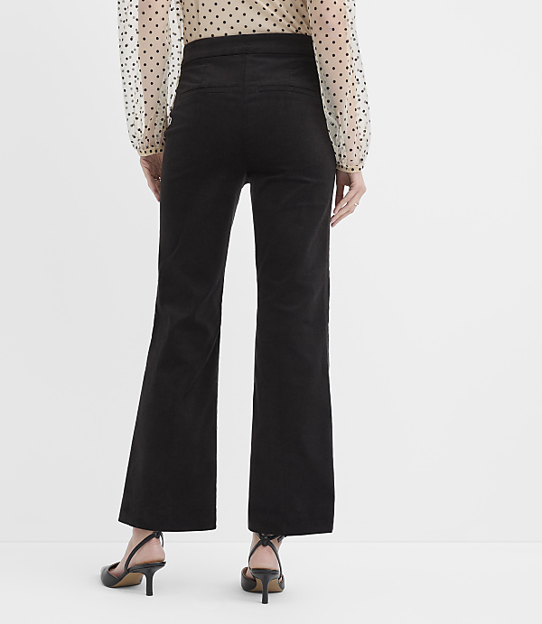 A person wearing a polka-dot blouse, black wide-leg trousers, and black heels stands against a plain white background.