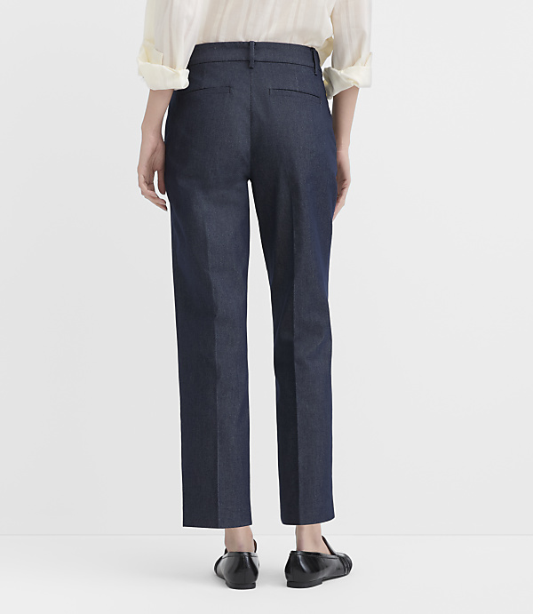 A person stands with their back to the camera wearing a cream blouse, dark blue trousers, and black flats against a plain white background.