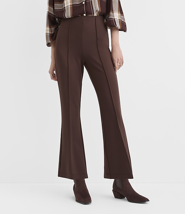 A person stands in brown flared pants and boots against a plain white background.