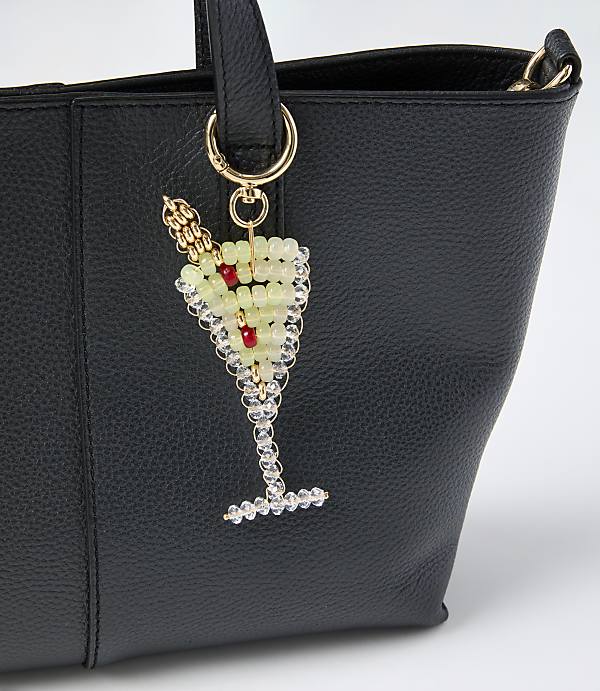 A beaded champagne glass charm hangs from the handle of a black leather handbag against a plain white background.