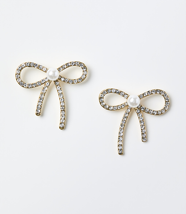 Two gold-toned bow earrings adorned with crystals and a central pearl rest on a plain white background.