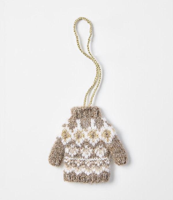 A small, knitted brown and white patterned sweater ornament with a gold string hangs against a plain white background.