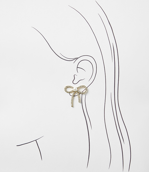 A gold bow-shaped earring with crystals sits on a simple line drawing of a woman's profile against a plain white background.