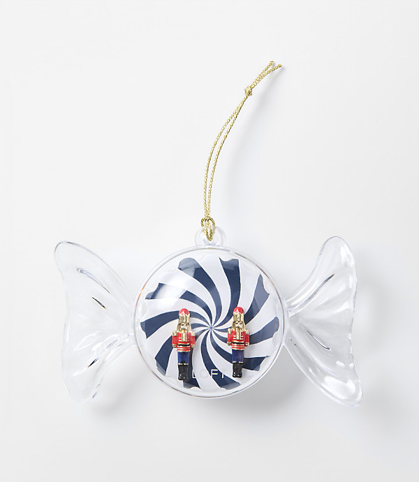 A clear candy-shaped ornament containing two small nutcracker figures against a blue and white swirl background, set against a plain white surface.