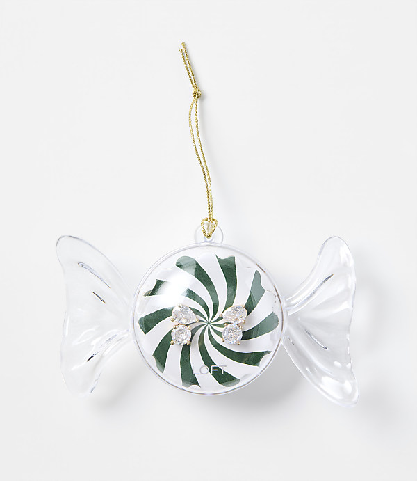A pair of sparkling stud earrings sits inside a candy-shaped clear plastic ornament with a green and white swirl background, set against a plain white surface.