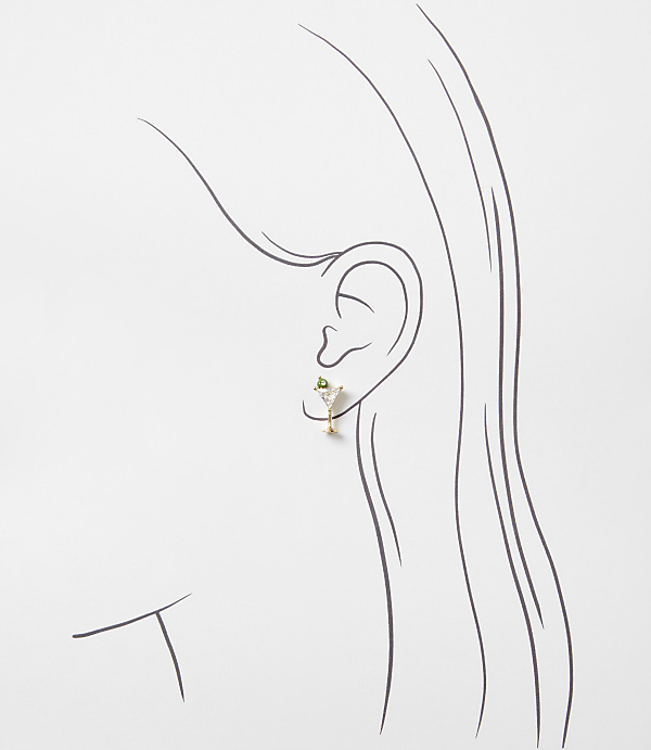 A small gold martini glass earring with a green gemstone sits on a minimalist line drawing of a woman's profile against a plain white background.