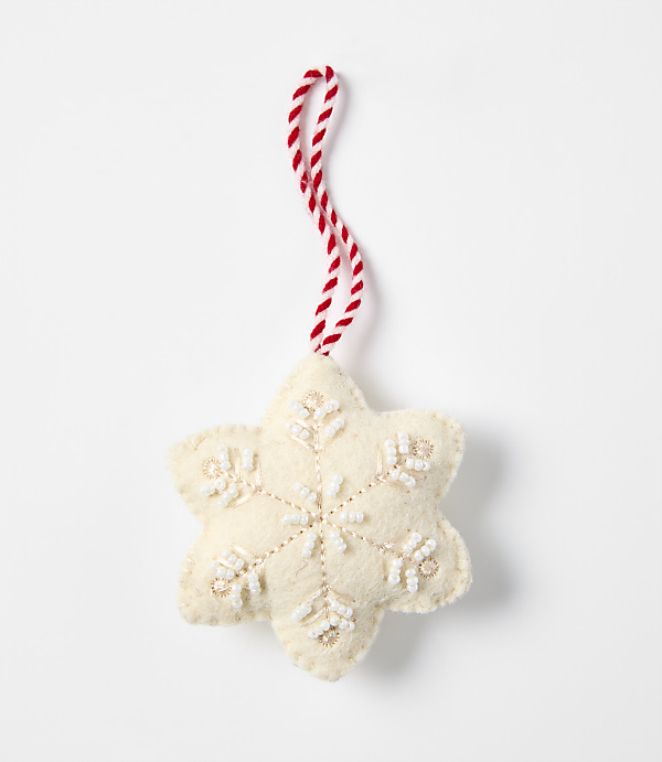 A cream-colored felt snowflake ornament with white bead accents and a red-and-white twisted string hangs against a plain white background.
