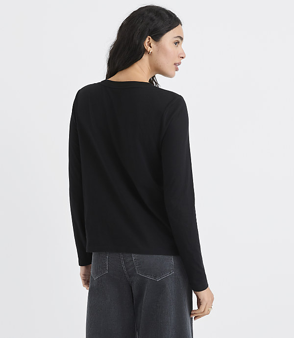 A woman wearing a black long-sleeved shirt and dark grey trousers stands against a plain white background.