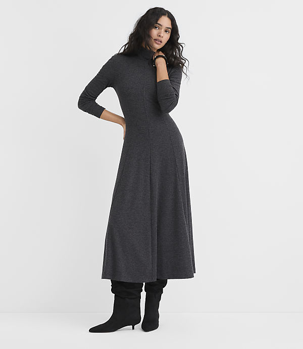A woman wearing a long-sleeved charcoal grey maxi dress and black boots stands against a plain white background.