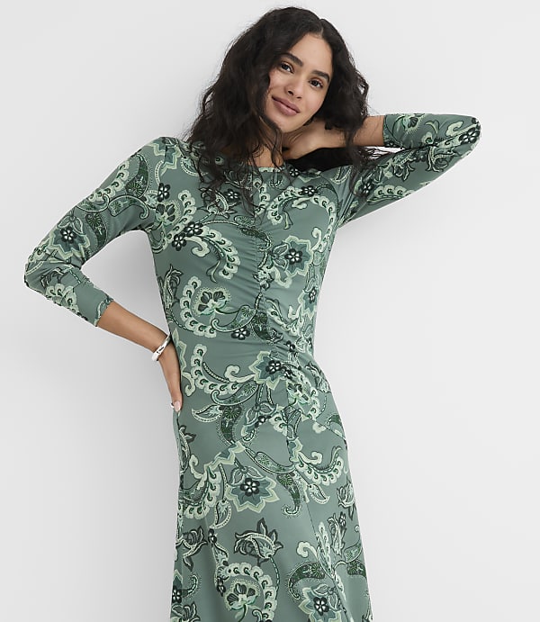 A woman wearing a green paisley print dress poses against a plain white background.