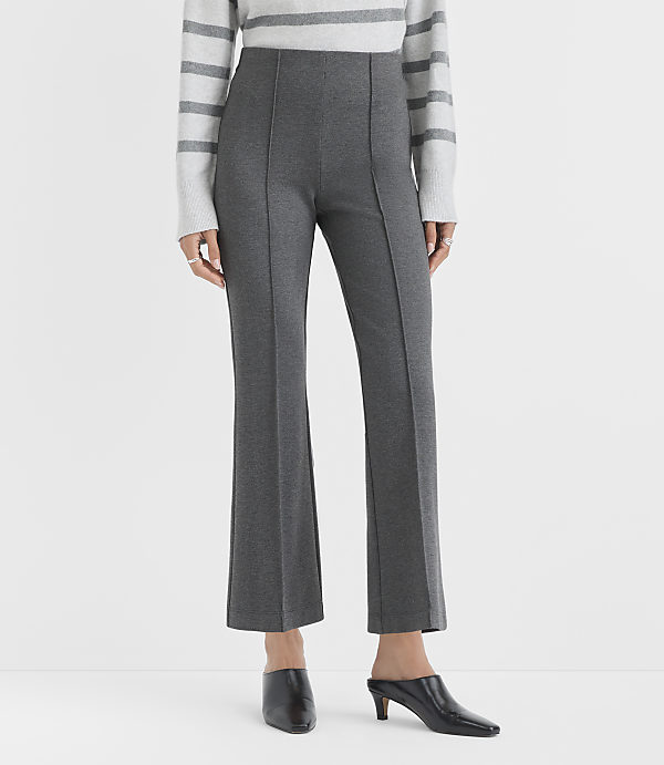 A person wearing a striped sweater, charcoal grey trousers, and black pointed-toe mules stands against a plain white background.