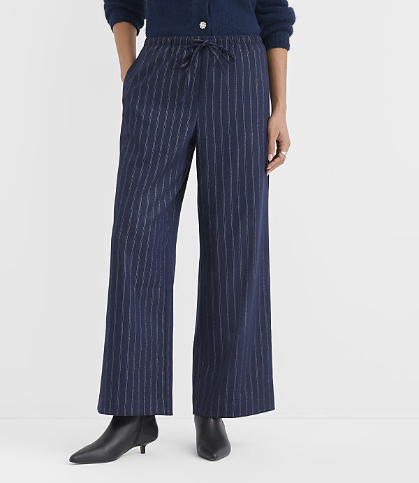 A person wearing navy blue pinstriped wide-leg pants and black pointed-toe heels stands against a plain white background.