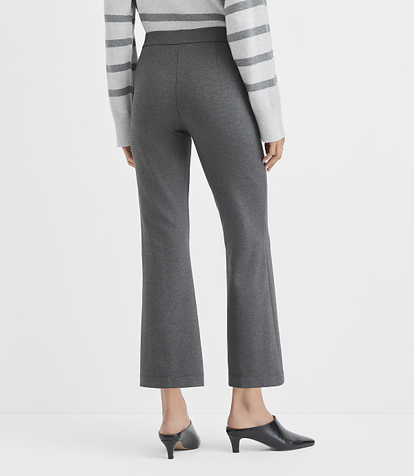 A person wearing a grey striped sweater, charcoal grey cropped trousers, and black mules stands against a plain white background.