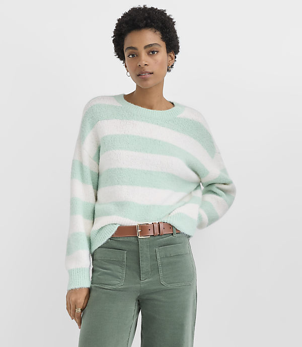 A woman wearing a mint green and white striped sweater and green trousers stands against a plain white background.