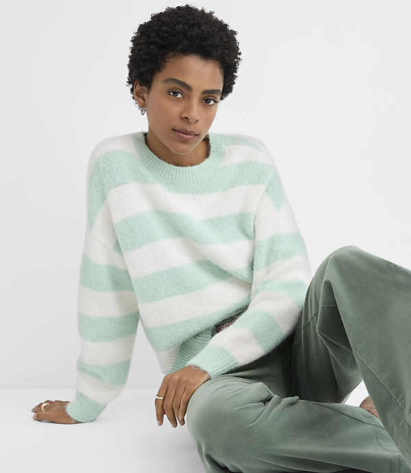 A woman wearing a mint green and white striped sweater and olive green pants sits against a plain white background.