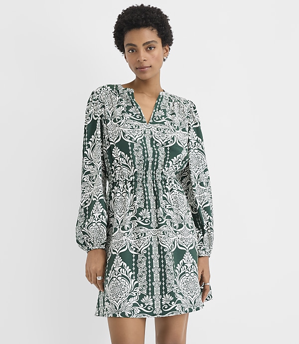 A woman wearing a green and white patterned mini dress stands against a plain white background.