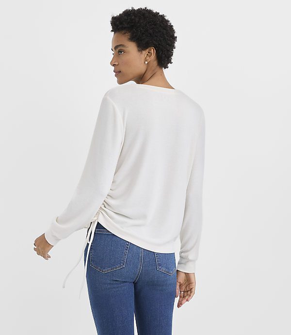 A woman wearing a white long-sleeved top and blue jeans stands against a plain white background.