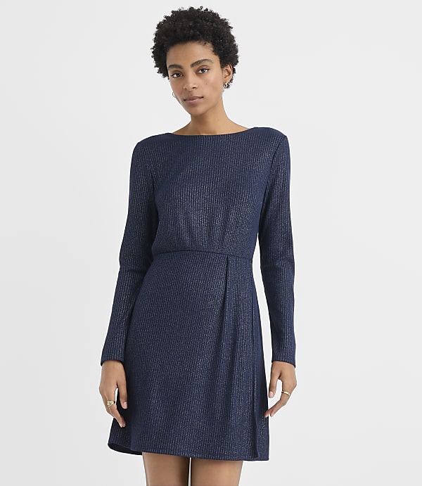 A woman wearing a navy blue ribbed long-sleeved dress stands against a plain white background.