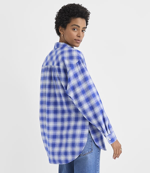 A woman wearing a blue and white plaid shirt and jeans poses against a plain white background.
