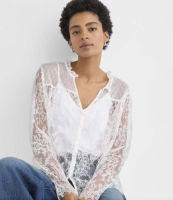 A woman wearing a white lace blouse and blue jeans poses against a plain white background.