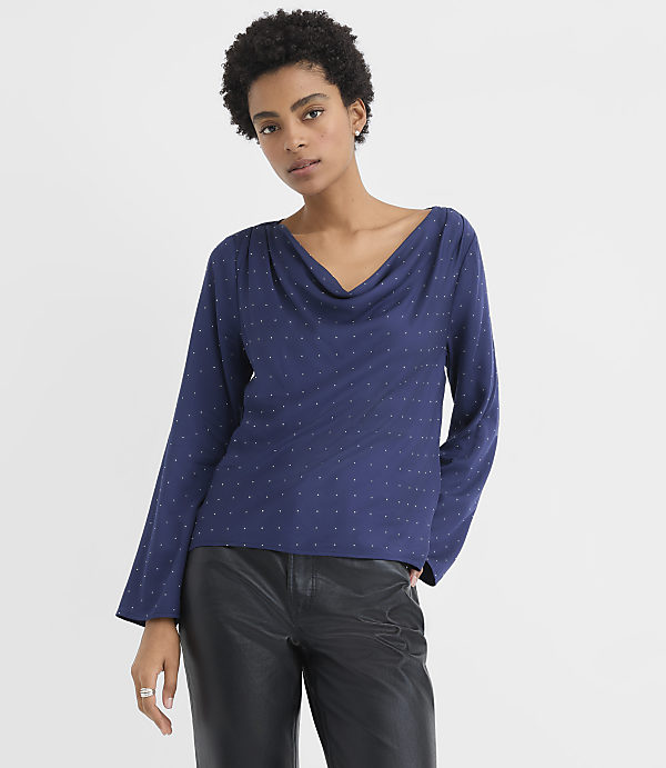 A woman wearing a navy blue polka-dot blouse and black leather pants stands against a plain white background.