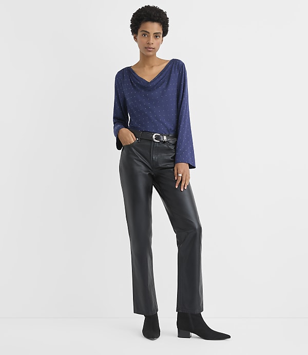 A woman wearing a blue polka-dot top and black leather pants stands against a plain white background.