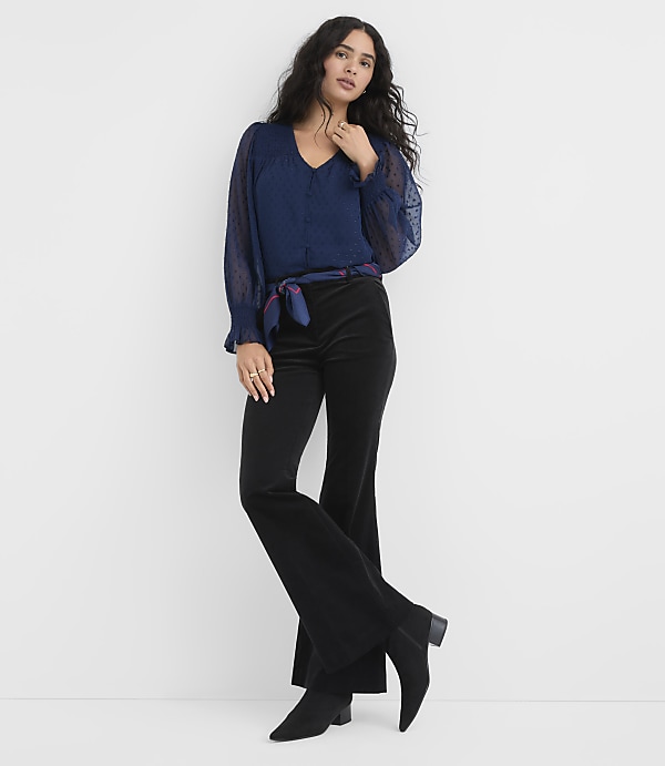 A woman wearing a navy blue blouse and black flared trousers stands against a plain white background.