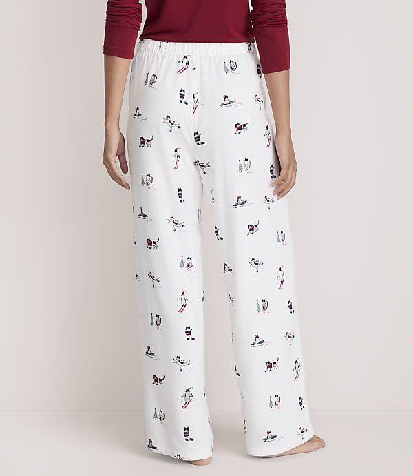 A person wears a red long-sleeved shirt and white pajama pants featuring a festive dog print, standing against a plain, light-colored background.