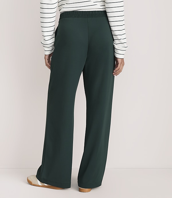 A person wearing a striped long-sleeve shirt and dark green wide-leg trousers stands against a plain, light-colored background.