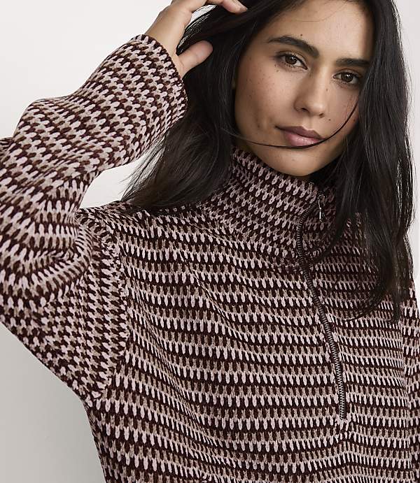 A woman wearing a patterned brown and cream quarter-zip sweater poses against a plain white background.