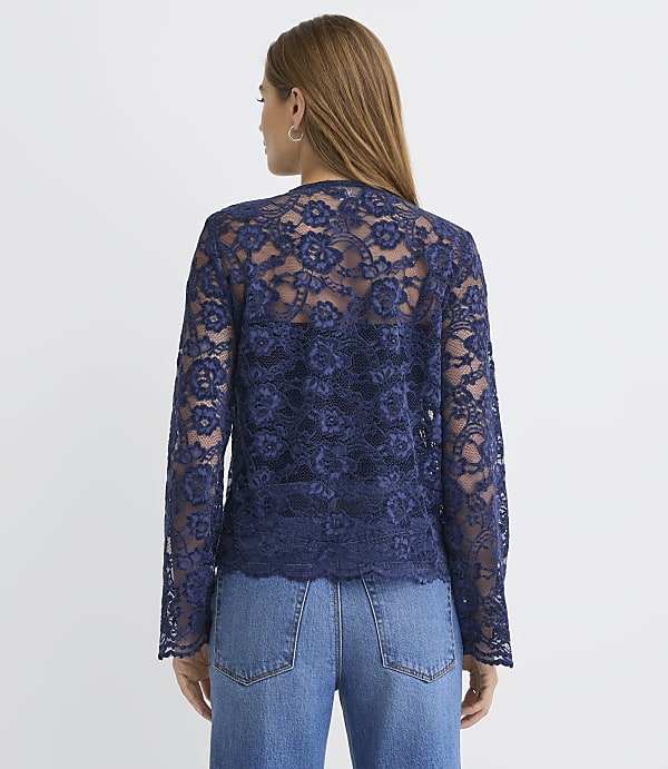 A woman wearing a navy blue lace top and blue jeans stands with her back to the camera against a plain white background.