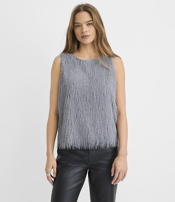 A woman wearing a grey shaggy sleeveless top and black leather pants stands against a plain white background.